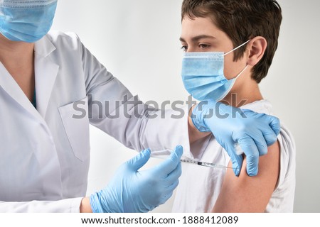 Close-up on hands in gloves with syringe and shoulder of the patient, teen kid. Covid 19, flu, tetanus or measles vaccine concept. Unrecognizable edic, doctor or nurse vaccinates school boy. Royalty-Free Stock Photo #1888412089