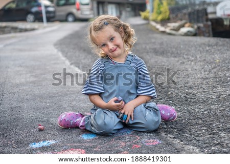 Little child is drawing picture with chalk on sidewalk after rain