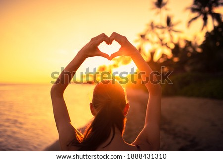 Female making heart shape hand in a beautiful sunset nature setting. Love and compassion concept. 