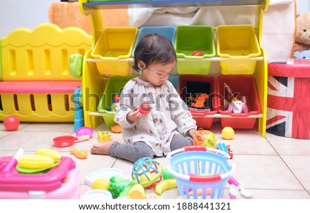 Cute Asian toddler girl child sitting on floor having fun playing alone in playroom at home, Little infant girl sitting W posture which is called W-sitting knees bent and feet positioned outside hips Royalty-Free Stock Photo #1888441321