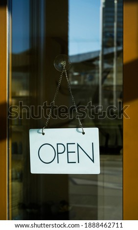 Close up of white  open sign hanging on glass door of cafe. Blurry background. Opened concept. 