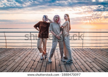 Dancing group of young talented freak women performing freestyle hip-hop moves. females enjoying modern dance expression. Outdoor training near sea or ocean during sunset. Royalty-Free Stock Photo #1888470097