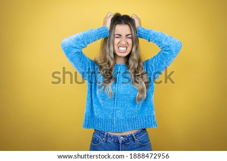 Pretty blonde woman with long hair standing over yellow background suffering from headache desperate and stressed because pain and migraine with her hands on head