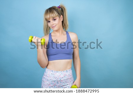 Young beautiful woman wearing sportswear holding a bottle of water over isolated blue background holding a dumbbells