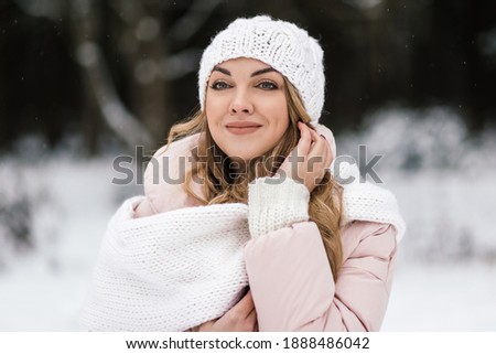 in a snowy forest, a beautiful girl smiles in a light hat and a trigger. portrait