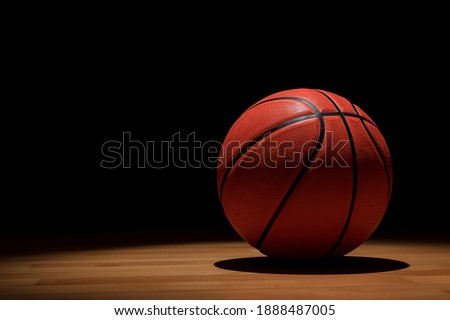 ISOLATED BASKETBALL ON WOODEN COURT WITH SPOTLIGHTS FROM ABOVE AND DARK BACKGROUND. TRAINING, MATCH AND CHAMPIONSHIP IN COLLEGE AND UNIVERSITY CAMPUS. SPORT BETS IN BETTING SHOPS. COPY SPACE. 