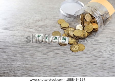 Block letters on plan with pile of coins flowing out from the container on the wooden table 