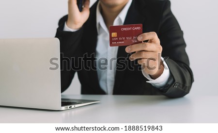 Businessman talking on the phone and reading credit card numbers while sitting at a cafe table and working.