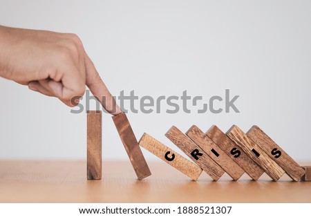 Stop crisis and risk management concept , Man using finger to stop wooden domino which falling to one wooden block still standing. Royalty-Free Stock Photo #1888521307