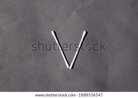 V letter sign by cotton bud stick, pure cotton on Grey background. Text element, lettering symbol in cotton bud. Cotton bud brand product.  Ear protection sticks  