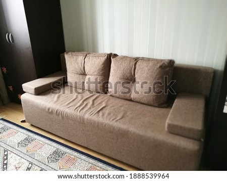 A soft caramel-colored sofa stands in the room between dark cabinets against a background of striped wallpaper Royalty-Free Stock Photo #1888539964