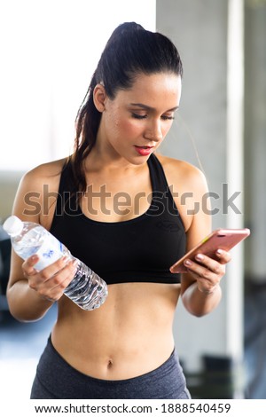 Active woman athlete taking rest and use smartphone after exercising at gym. Fitness Healthy lifestye and workout at gym concept.