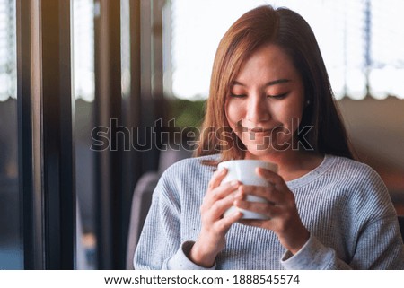 Closeup image of a beautiful young asian woman holding and drinking hot coffee in cafe