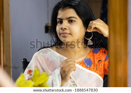 a beautiful Indian woman in white saree wearing silver earrings in front of mirror with smiling face
