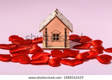 Wooden toy house and red hearts on pink background. Sweet home or gift for valentine's day concept. Mortgage concept. Eco-friendly house. Copy space for text