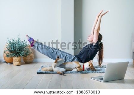Doga or Doga yoga is the practice of yoga as exercise with dogs. Young woman in yoga position balancing with her dog. Home online training with a pet Royalty-Free Stock Photo #1888578010