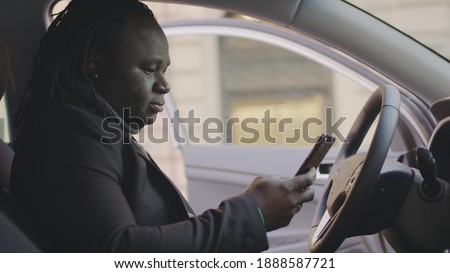 Successful african american man getting surprised text message while sitting on drivers seat of his car. High quality photo