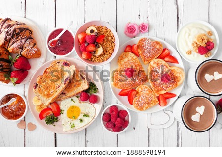 Valentines or Mothers Day brunch table scene. Top view on a white wood background. Heart shaped pancakes, eggs and an assortment of love themed food. Royalty-Free Stock Photo #1888598194
