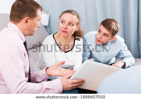 Smiling middle-aged mother and son signing agreement papers at home