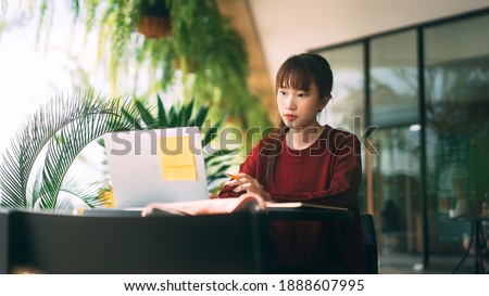 Young adult asian college student woman wear red sweater. Using laptop study and work online at cafe. University people city lifestyle at outside from home on winter day. Royalty-Free Stock Photo #1888607995