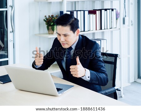 Handsome Asian businessman in suit looking at screen and showing thumb up to laptop computer, video call, meeting online working, video conference. Social distancing or telecommunication work concept.
