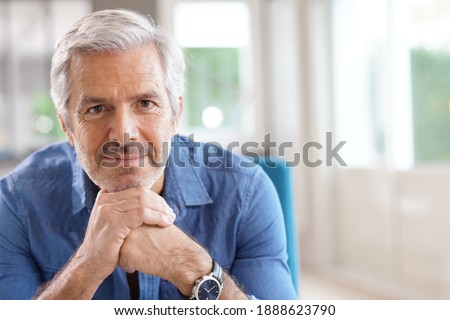 Portrait of 60-year-old man with grey hair and blue shirt looking at camera Royalty-Free Stock Photo #1888623790