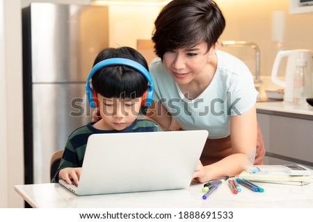At-home learning, new normal daily routine for kids. A smart asian boy using laptop computer to study from home during Covid-19 pandemic lockdown with his mother. Online education, Homeschooling. Royalty-Free Stock Photo #1888691533