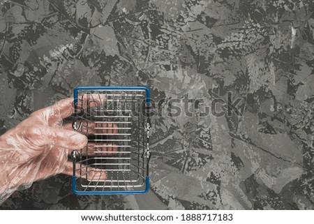 The hand of a man in a disposable glove holds a small basket for food