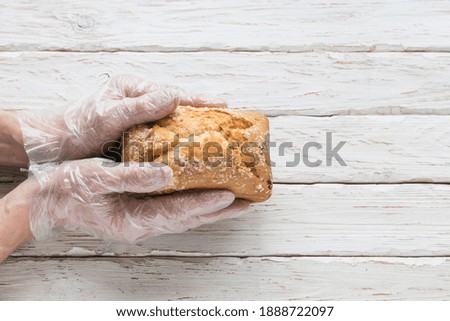 Men's hands in protective gloves hold a loaf of bread on a light decorative background