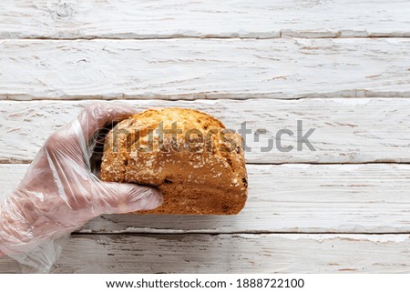 Men's hands in protective gloves hold a loaf of bread on a light decorative background