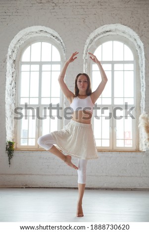 A slender girl ballerina is dancing in a light hall.