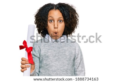 Young little girl with afro hair holding graduate degree diploma scared and amazed with open mouth for surprise, disbelief face 