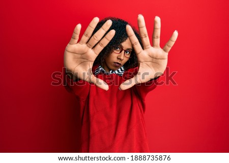 Beautiful african american woman with afro hair wearing sweater and glasses doing frame using hands palms and fingers, camera perspective 
