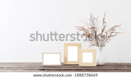 frame and dried flowers in white vase on old wooden shelf