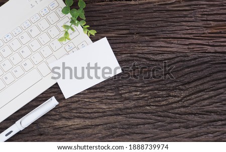 White business card over keyboard and pen, little tree on wood office desk table. Top view with copy space. flat lay.

