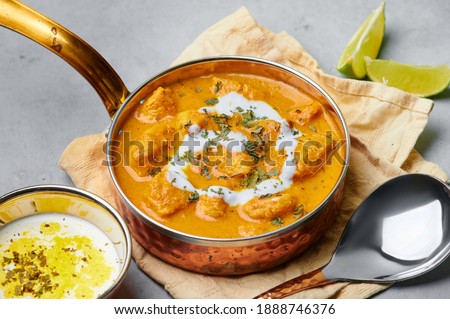 Murgh Makhani or Butter Chicken in copper bowl on gray concrete table top. Indian Cuisine dish with chicken meat and creamy masala. Asian food and meal. Close up Royalty-Free Stock Photo #1888746376