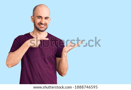 Young handsome man wearing casual t shirt amazed and smiling to the camera while presenting with hand and pointing with finger. 