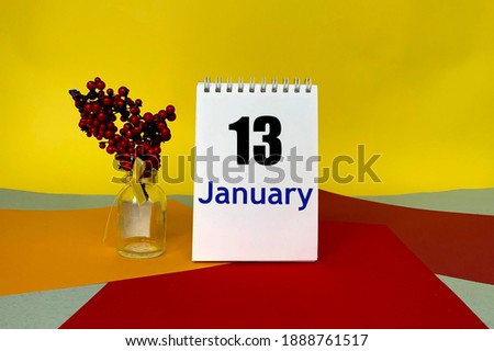January 13 on a notepad on a multi-colored background.Next to it are red berries in a bottle .Calendar for January .