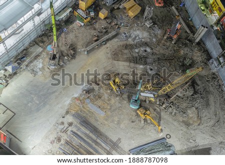 Aerial view of busy industrial under construction site workers working with cranes and excavators. Top view of precast concrete slap floor. Development high rise architecture building at night.
