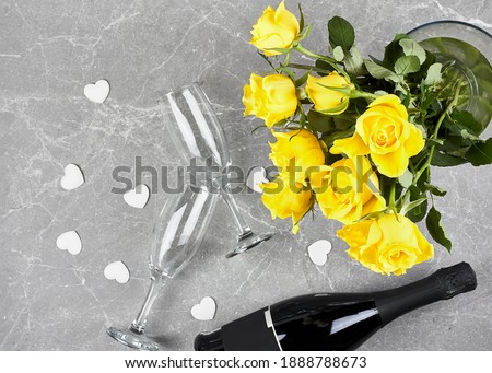 Yellow roses, bottle of wine, champagne flute and white hearts on gray background. Flat lay. Copy space. Valentines day, Mothers day, Womens day, gift, holiday, dating concept.