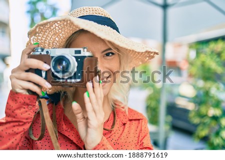 Young blonde tourist woman smiling happy using vintage camera walking at the city.