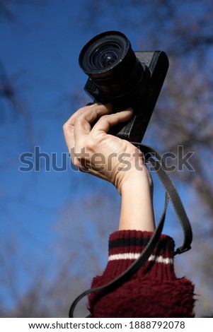 woman hand holding a 35mm camera with sky background and trees in winter