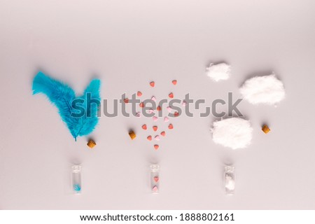 Conceptual arrangement with beautiful blue feathers, pastel pink hearts, fluffy white cotton clouds, potion bottles and corks against a classy modern gray background. Flat lay.