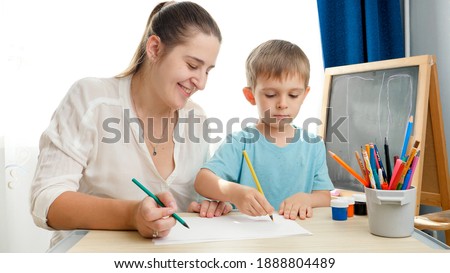 Smiing young mother drawing picture with her little son with pencils. Concept of parenting and education at home. Creativity and children art.