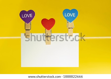 White paper plaque with space for text with heart-shaped clothespins on a cord. Bright yellow background. Mock ap. Valentine's day.