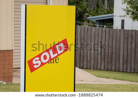 Yellow for sale sign near the resedential building house with sold sticker on it
