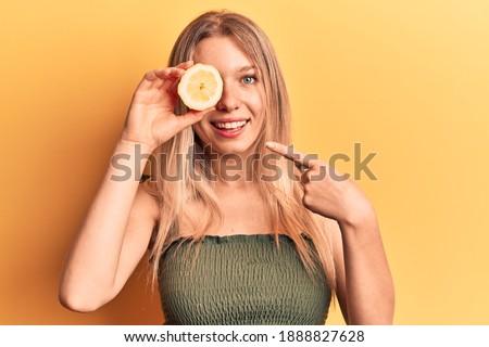 Young blonde woman holding lemon smiling happy pointing with hand and finger 