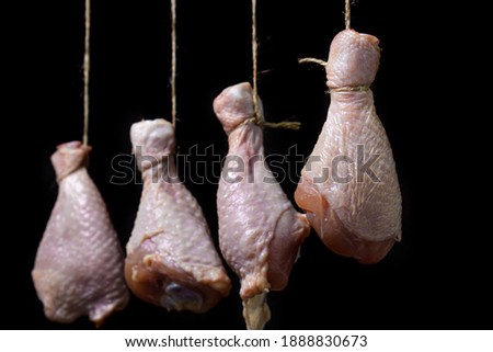 Raw chicken legs on a black background. Chicken legs hang suspended by a thread. Chicken meat.