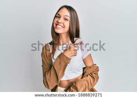 Young brunette woman wearing casual clothes smiling cheerful pointing with hand and finger up to the side 