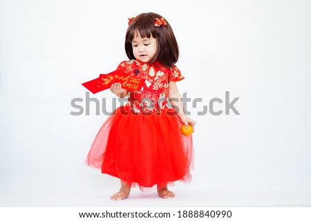 An asian cute baby girl in Chinese traditional costume holding the red lucky envelopes and sacred orange in Chinese New Year on white background (Chinese translation : Lucky and happiness)